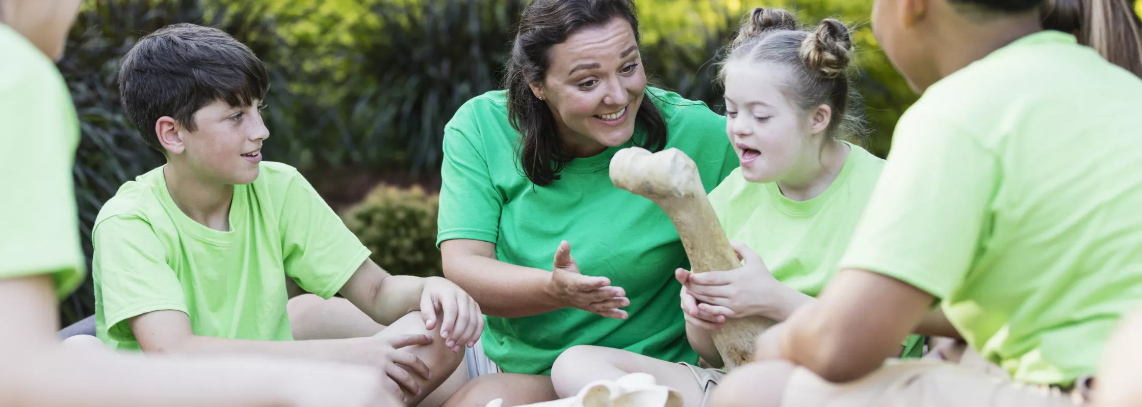 Kind mit einer sichtbaren kognitiven Beeinträchtigung (Trisomie 21)  in einer Gruppe von Kindern und einer erwachsenen Frau im Freien